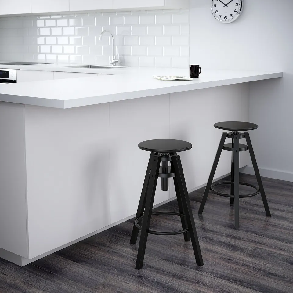 Two black adjustable bar stools beside a modern white kitchen counter with a clock.