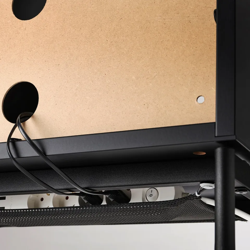 Black tv stand with glass doors, cable management net visible underneath, and adjustable feet for uneven floors.
