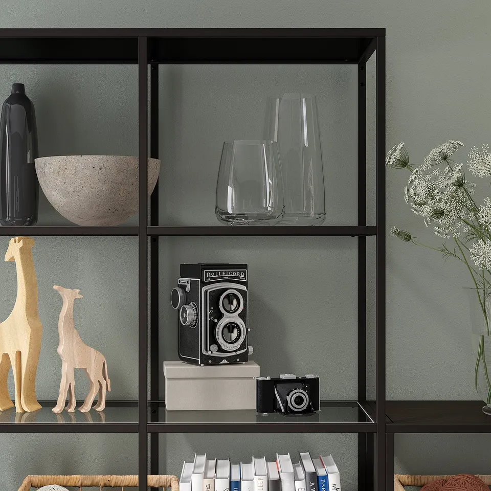 Shelf with glass panels decor items like vases, wooden giraffes, and vintage cameras. Adjustable feet ensure stability on uneven floors.
