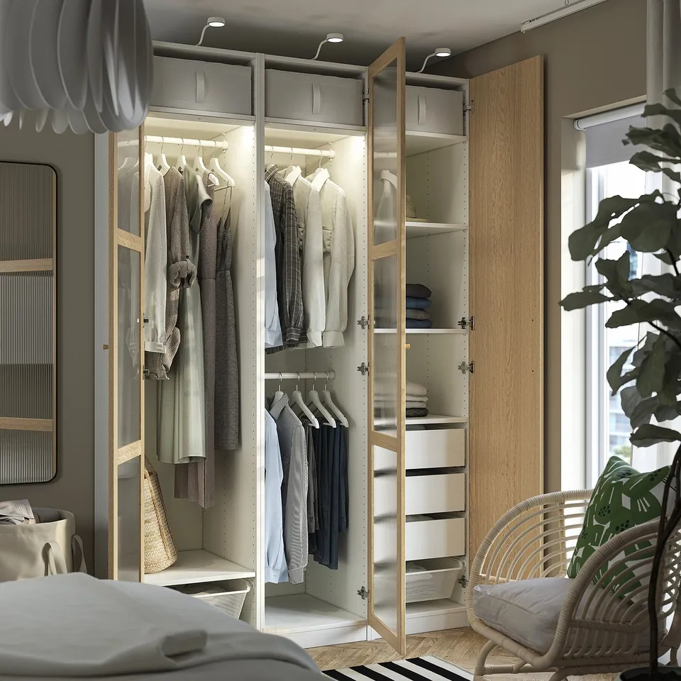 Open wardrobe displaying clothes, with integrated lighting and shelves. It includes hanging space, drawers, and a mesh basket for storage.