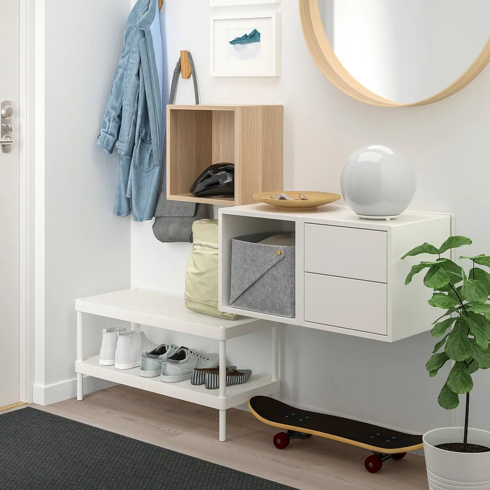 Modern, minimalist entryway with white EKET storage. Wooden shelving, hanging hooks, and a skateboard.