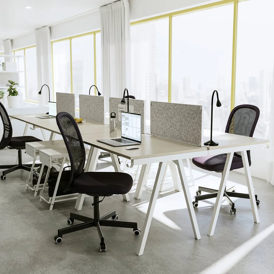 Modern office space with trottten white desks and black chairs, featuring large windows and natural light.