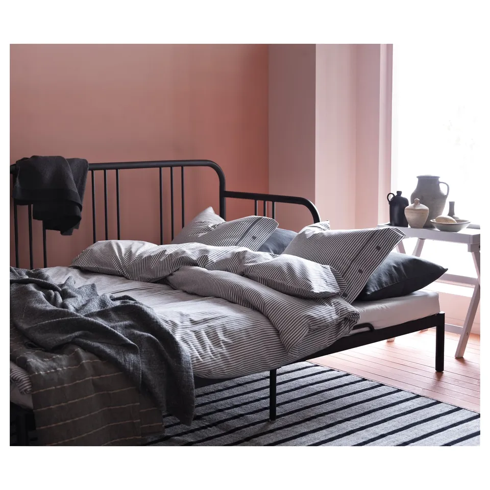 Black metal day-bed with striped bedding, black throw, against pink walls.