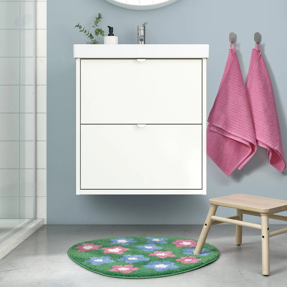 Bathroom with white VATTENSKRUV mat, pink towels, and wooden stool. Mat is green with pink and blue flowers, soft, recycled polyester.