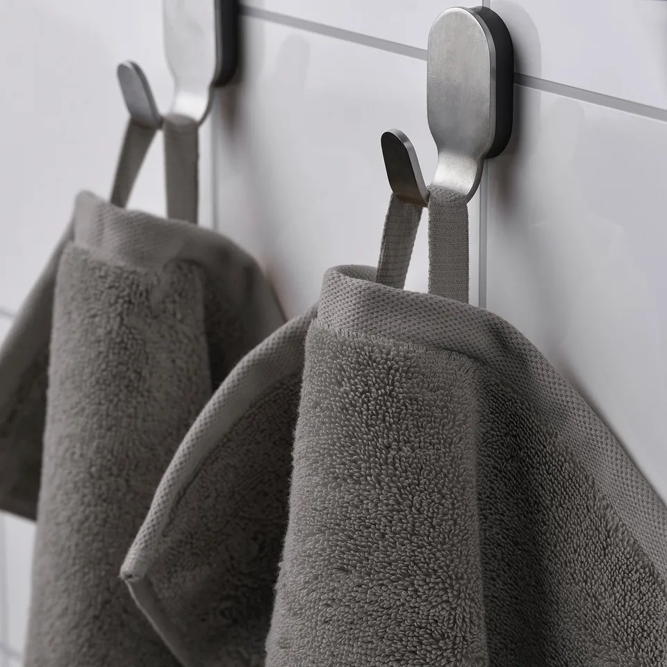 Two grey towels hang on metal hooks against a white wall, showcasing absorbent and soft fabric.