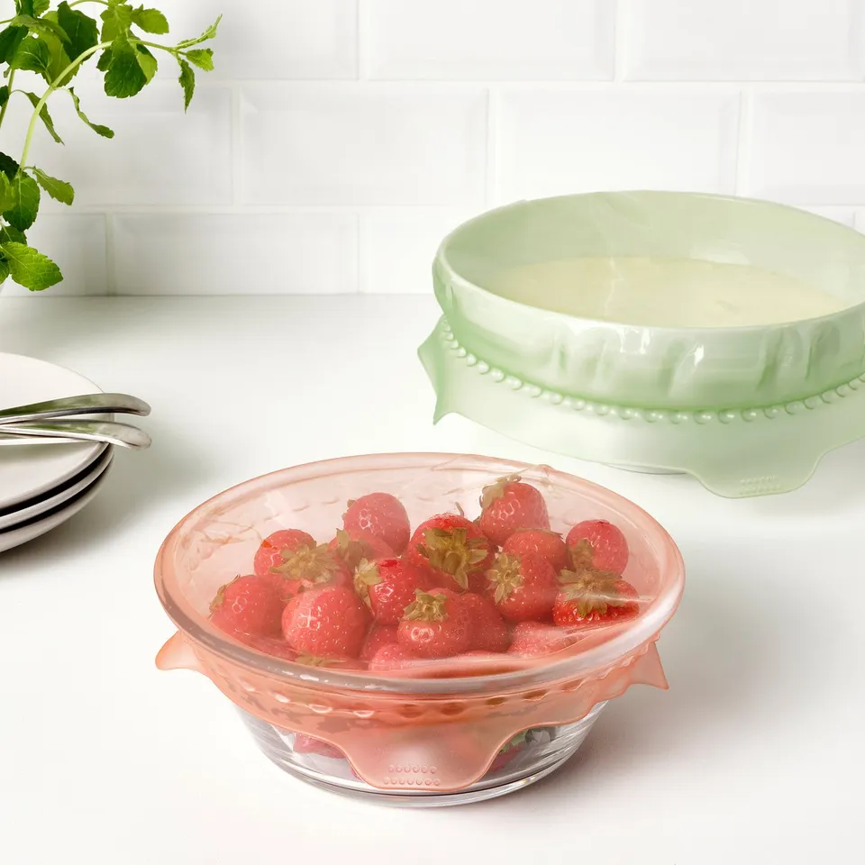 Two glass bowls with strawberries and custard on a counter, covered with reusable lids.