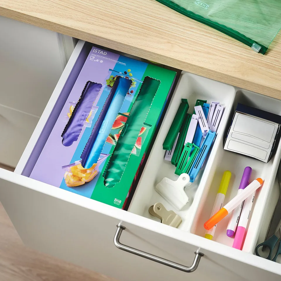 Open drawer with organizedoffice supplies, assorted pens, markers, clips, and resealable bags.