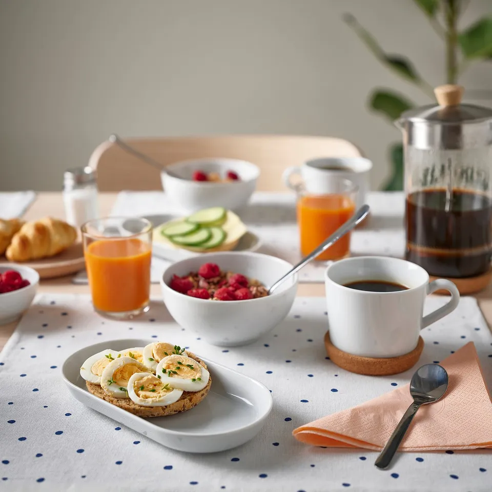 IKEA 365+ white porcelain plate set, featuring varying sizes and a simple design, stacked on a polka dot tablecloth with breakfast items.