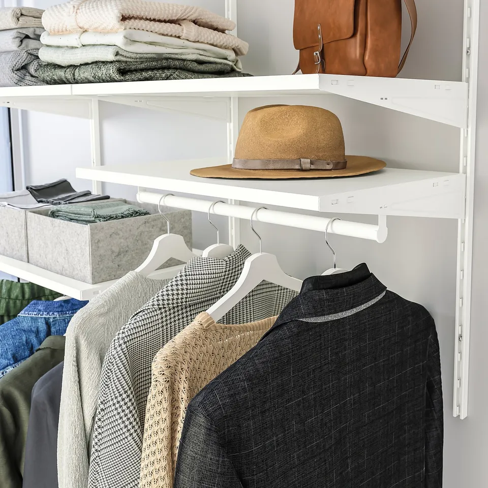 Organised closet with hanging sweaters, jackets, and a hat on top shelf, utilising efficient storage solutions.