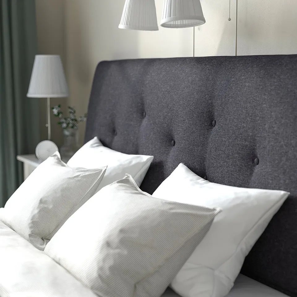 Bed with grey headboard, white pillows, lamps, and green curtain.