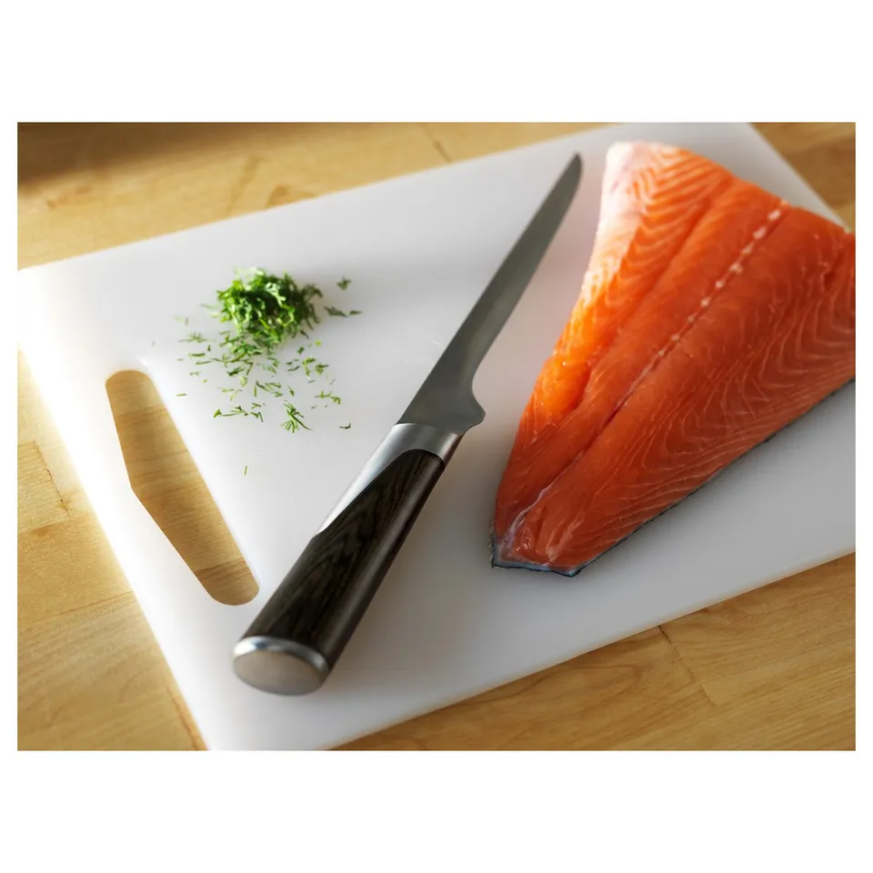 A white cutting board holds a knife and fresh salmon fillet, ready for meal prep.