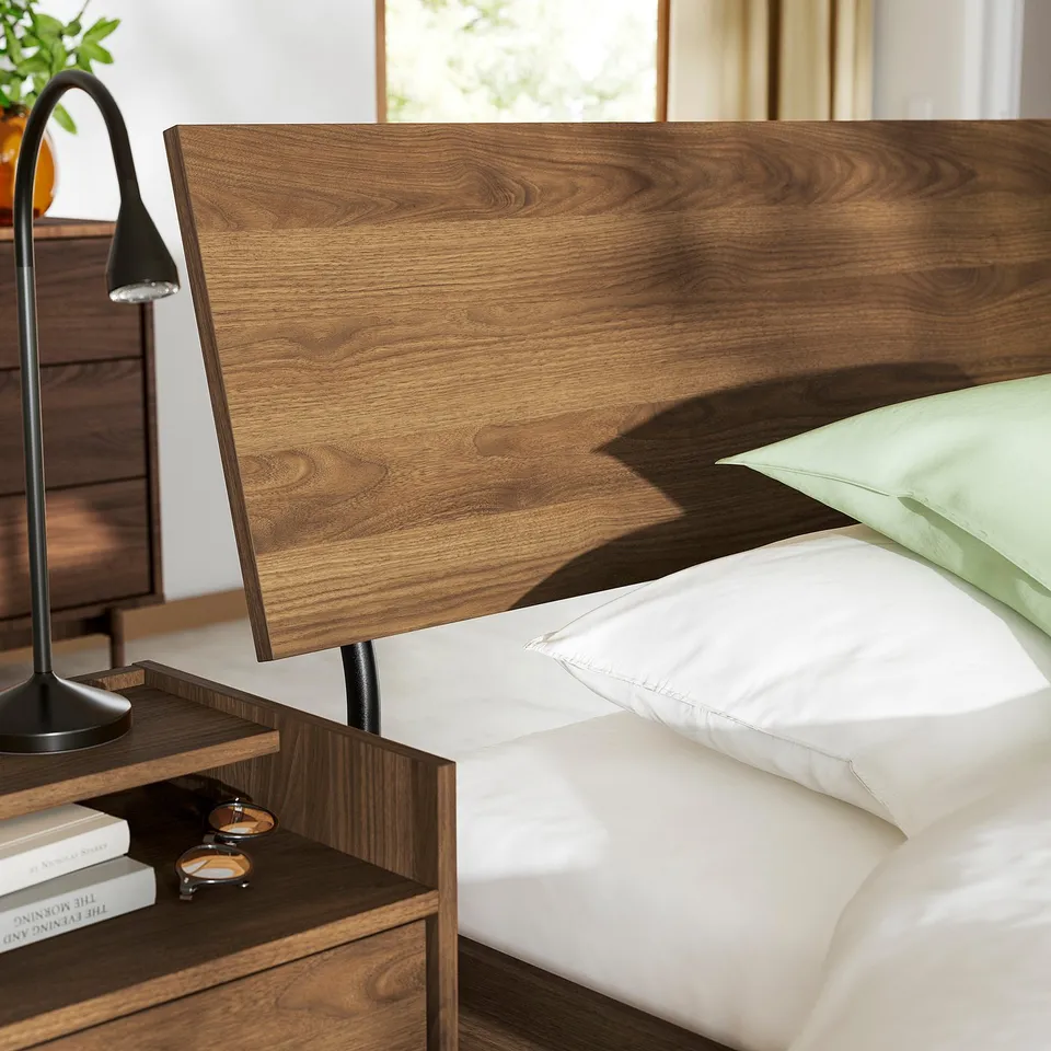 Wooden bed with walnut tone, lamp, books, and glasses on bedside table.