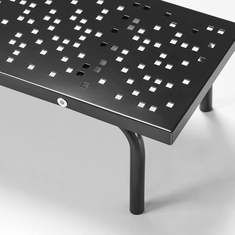 Black metal desk with perforated surface, supported by two cylindrical legs.
