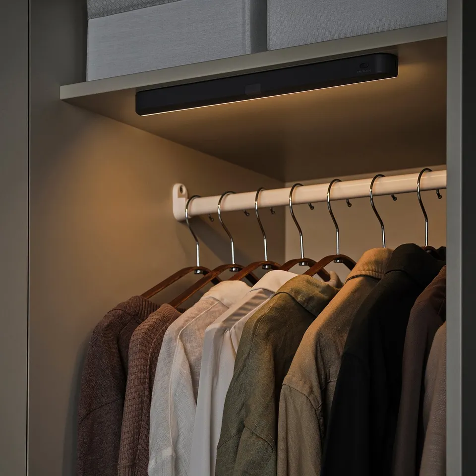 Closet with KÖLVATTEN motion-activated light. Clothes hang below warm glow.