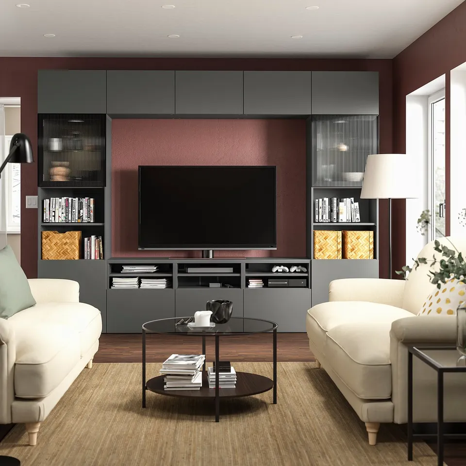 Modern living room with red walls a BESTÅ tv bench in grey, two white sofas, and glass coffee table with books and remote.