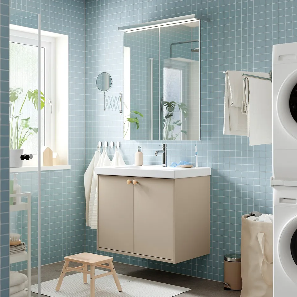 Modern bathroom with blue tiles, beige vanity, sink, mirror, and towels. Washing machine nearby.