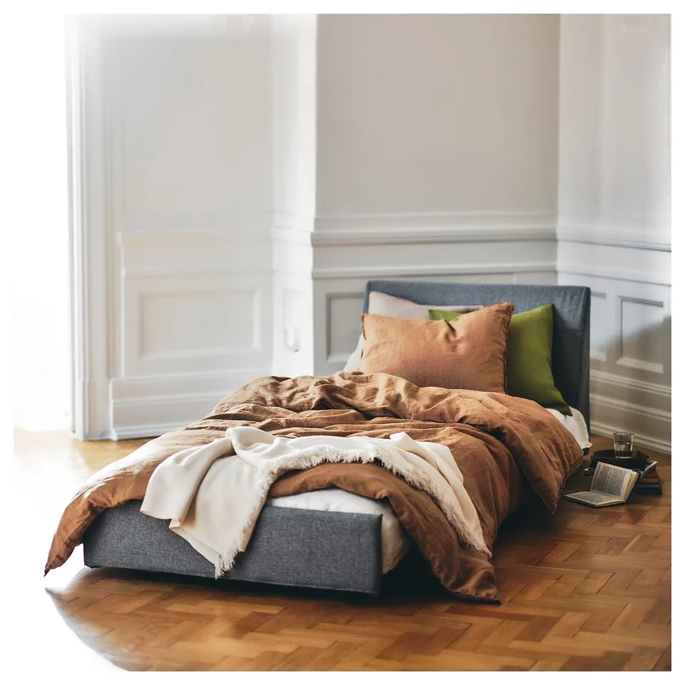 Cosy bedroom with a grey KIVIK sofa-bed, brown blankets, and colourful pillows. Laptop on nearby wooden floor.