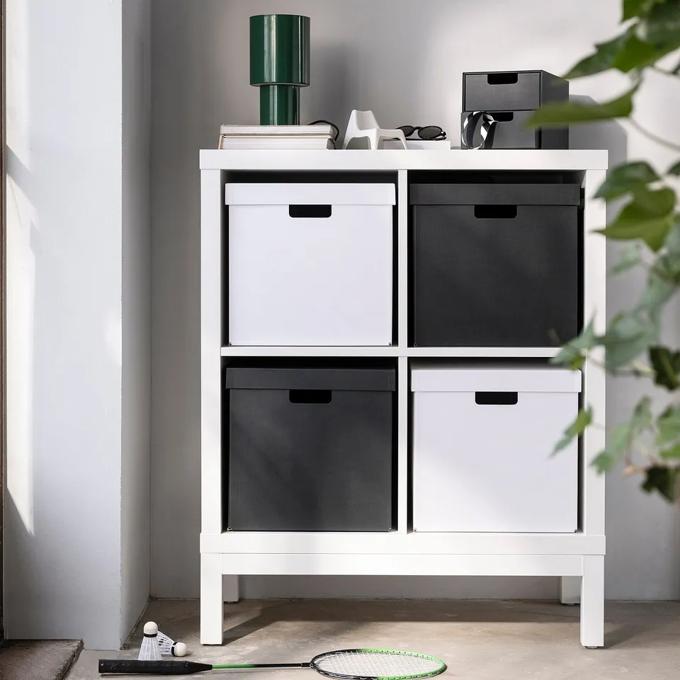 White storage box on shelf, made of recycled paper, holds items, larger than racket beneath.