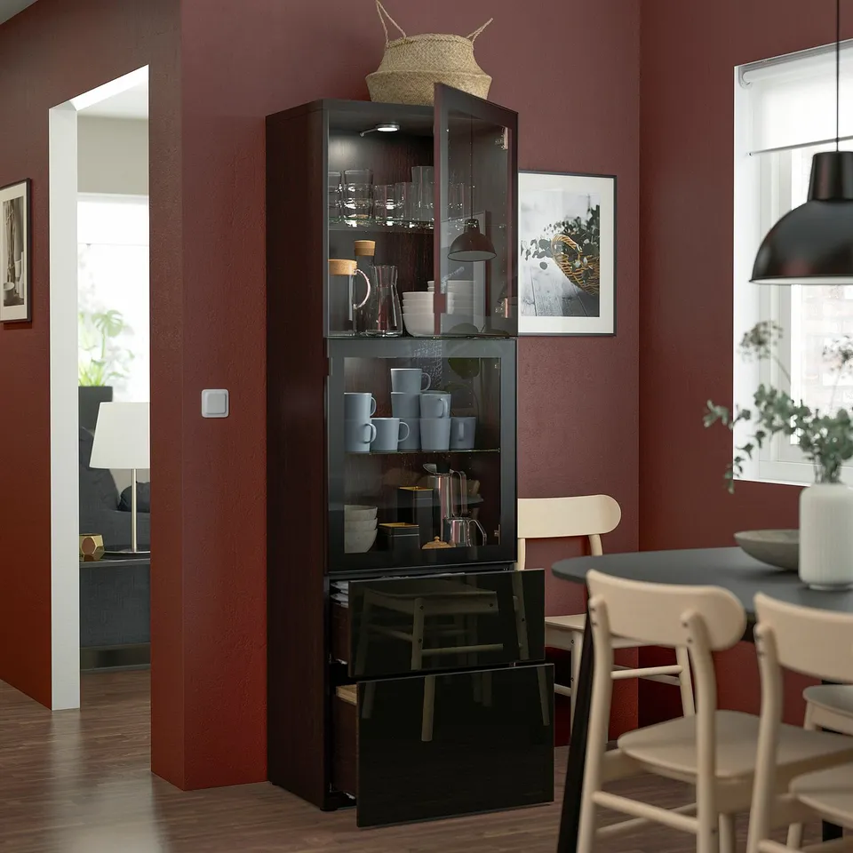 Dark wooden glass-door cabinet items, stores more inside. Placed against red wall, near dining area with chairs.