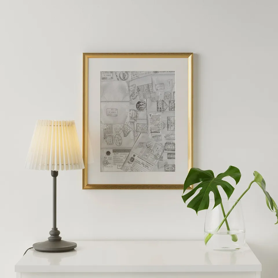 Framed ticket collage on wall, between lamp and plant, gold finish.
