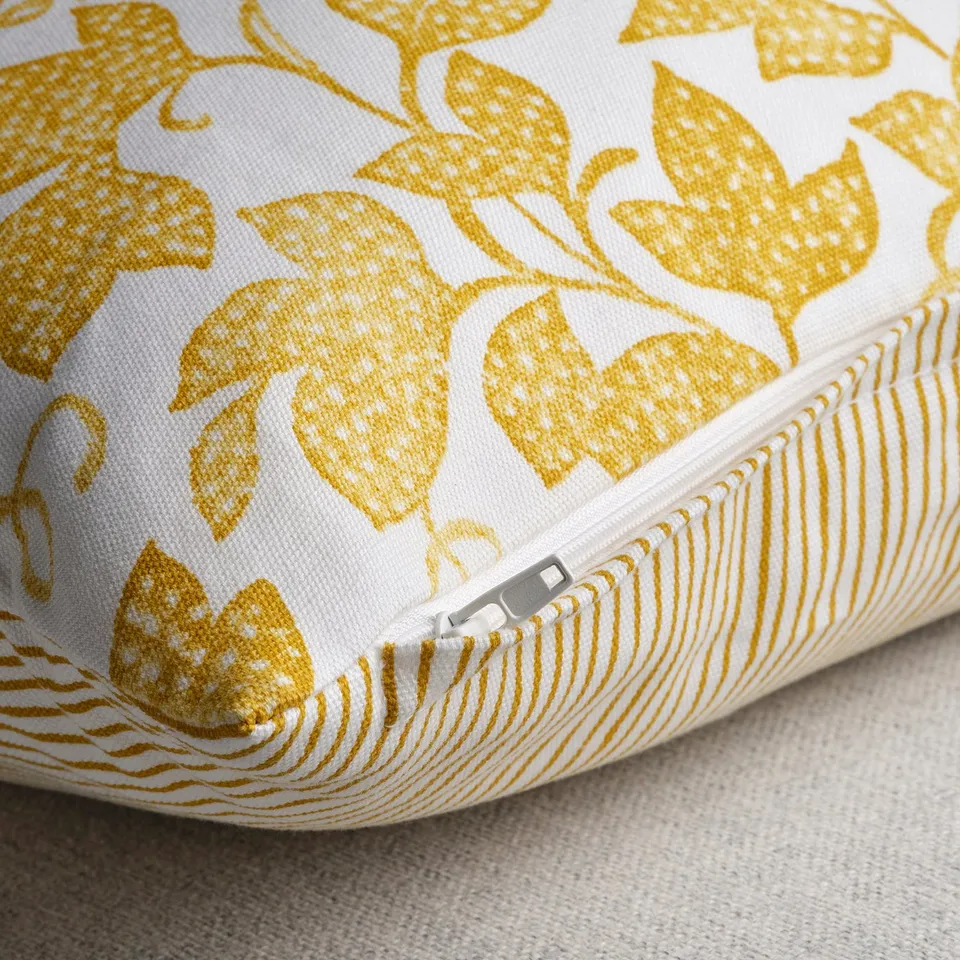 Yellow floral pillow, white background, visible zip, elegant design.