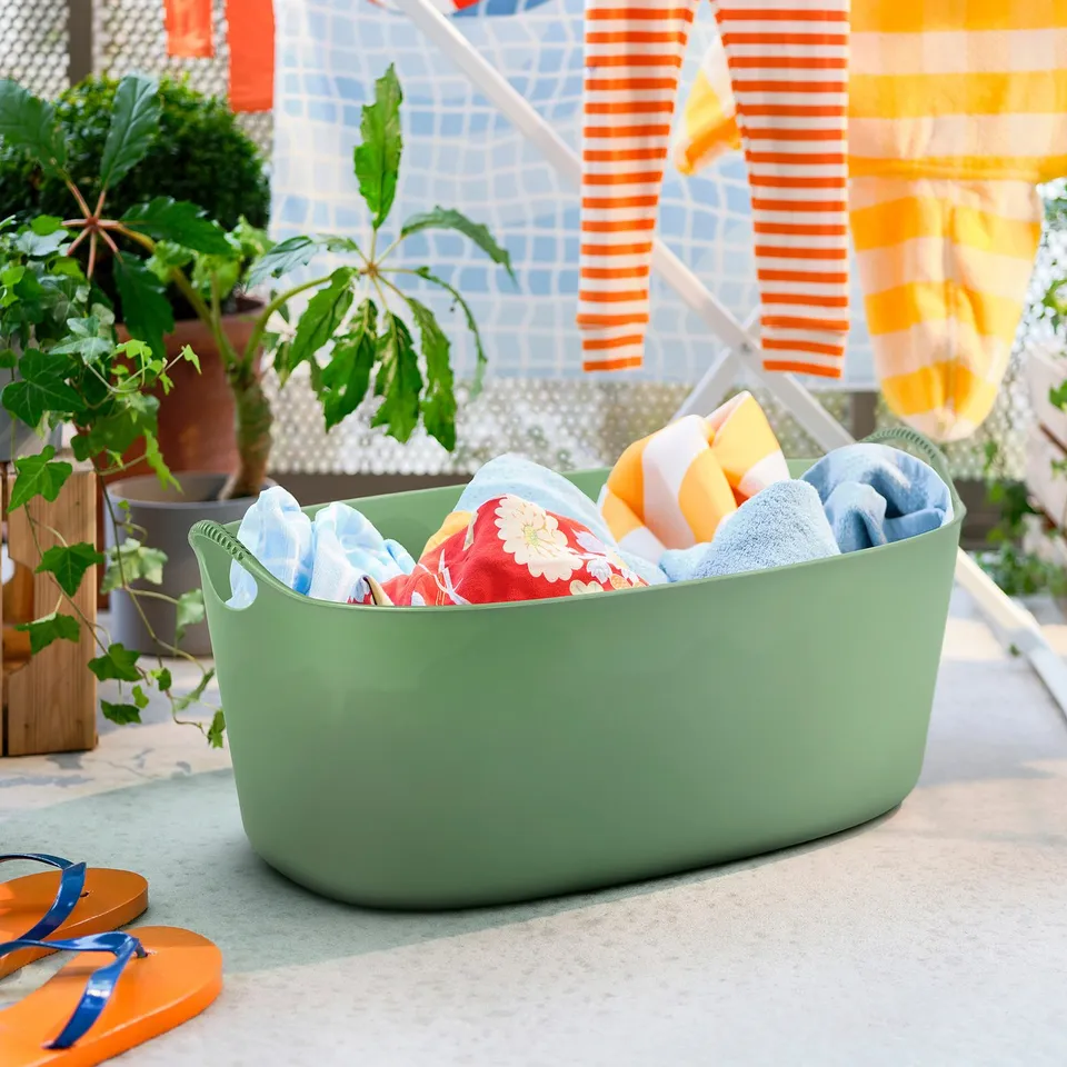 Green TORKIS laundry basket with towels, by mosaic wall.
