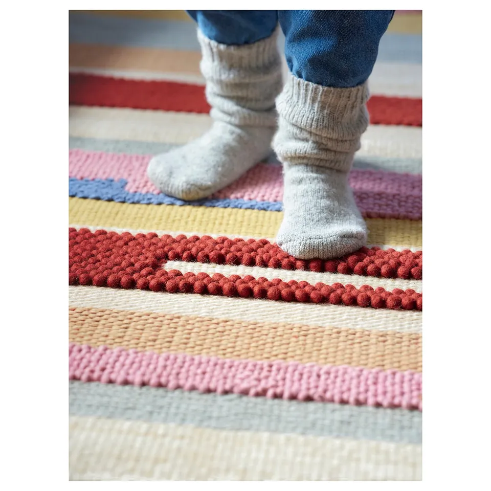 A childs feet on a handwoven, multicoloured rug with red and pink stripes.