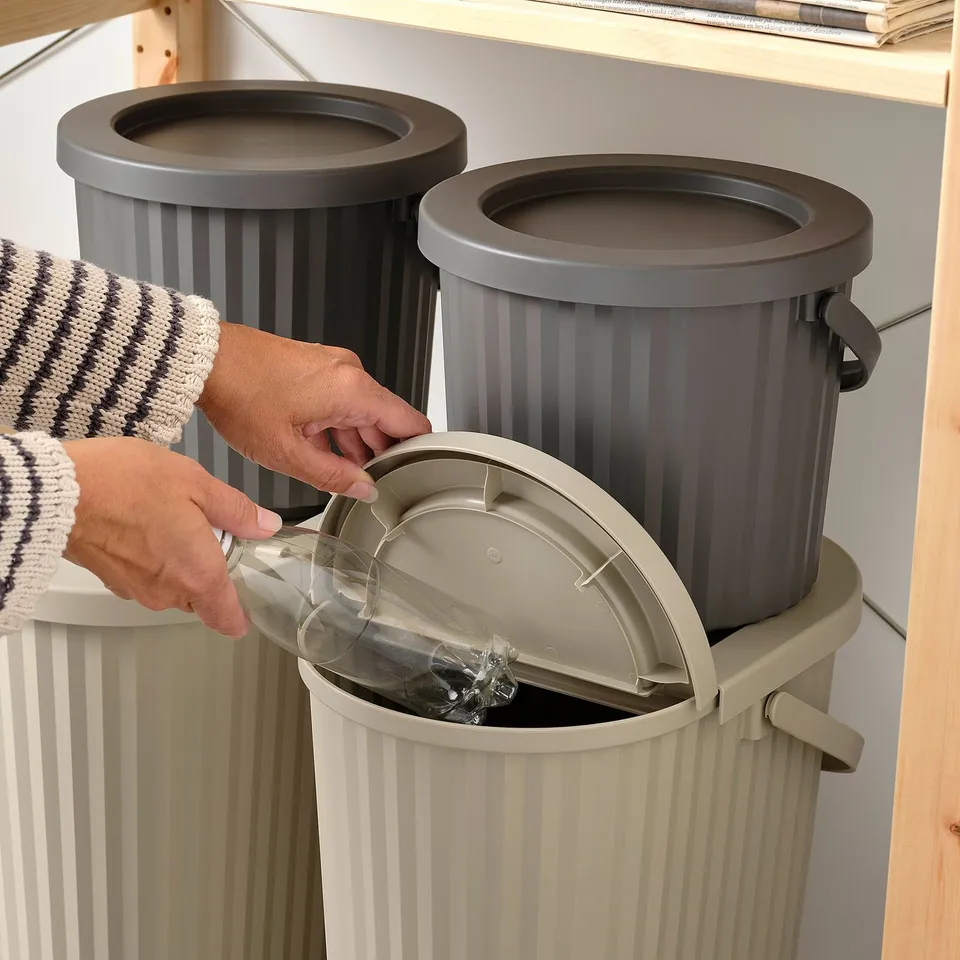 Person empties plastic bottle into grey DAMMÄNG recycling bin with lid open.