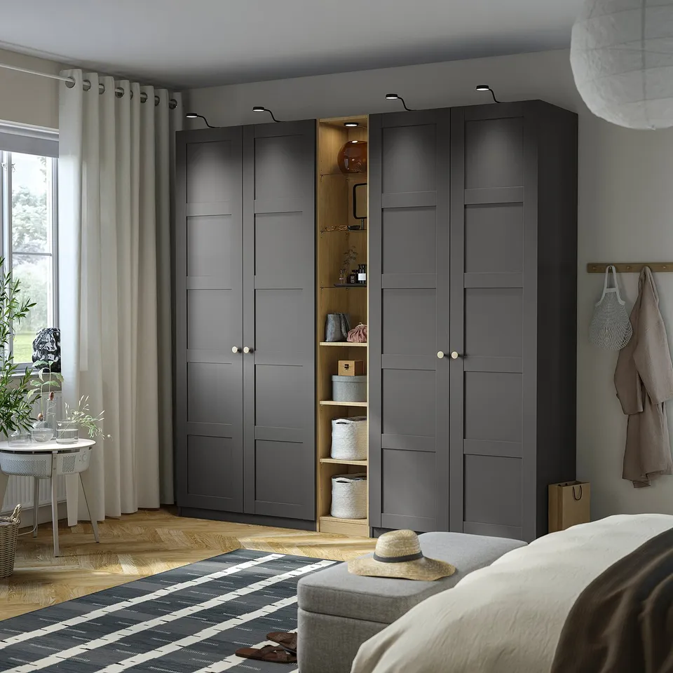 Modern bedroom with tall dark grey PAX wardrobe, mixed shelves, bed, rug, table with jacket.