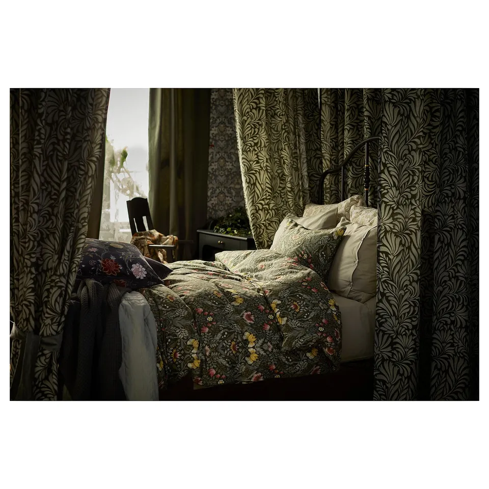 Bed with floral quilt, green curtains, lamp, chair, and plant.