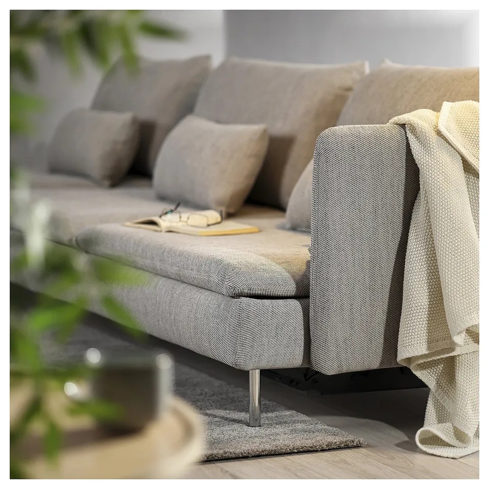 Grey SÖDERHAMN sofa bed with wooden legs, cushions, and a blanket. A book rests on the seat in a softly lit room.