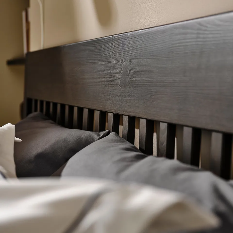 Modern bed with dark wood headboard and slatted footboard, showing cosy grey bedding.
