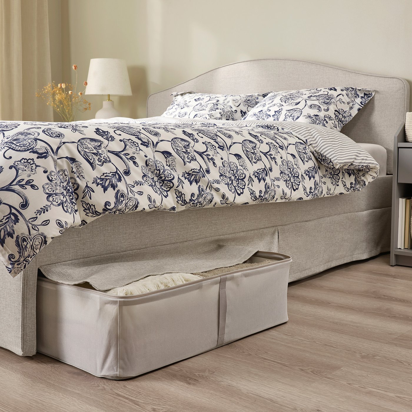 Grey bed, curved headboard, washable cover, bed skirt, bedside table with lamp.
