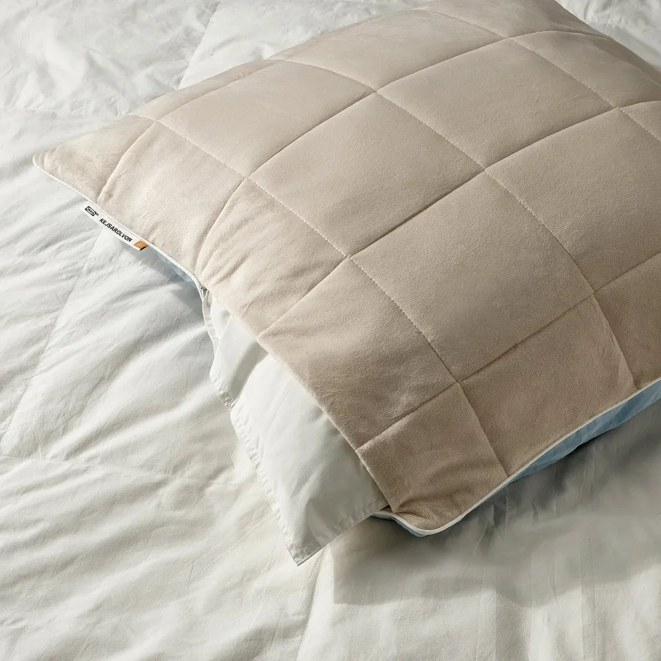 Beige pillow protector on a bed, offering warmth and comfort. Visible tag reads KEJSAROLVON.