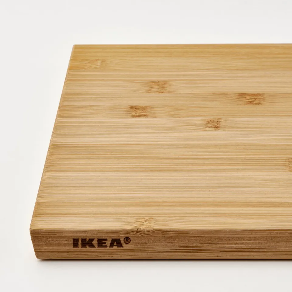 Light, natural bamboo cutting board with smooth surface, slanted edges, and IKEA branding for easy grip and use.