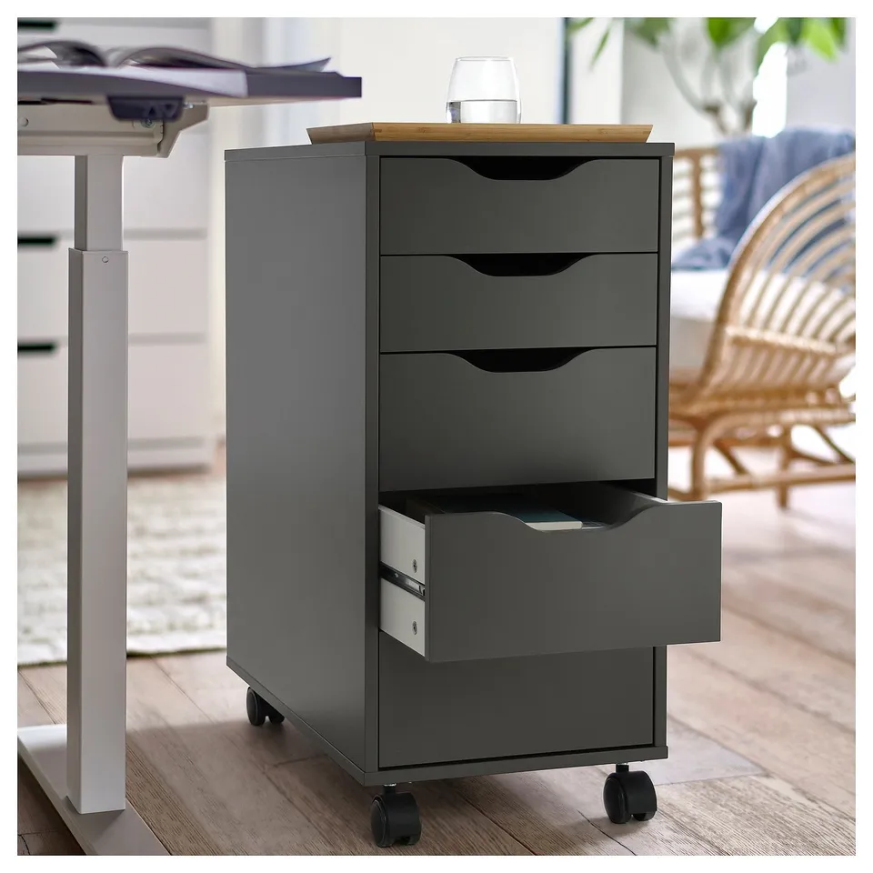 A grey ALEX rolling filing cabinet with four drawers, a wooden top, and wheels. It is placed under a desk in an office setting.
