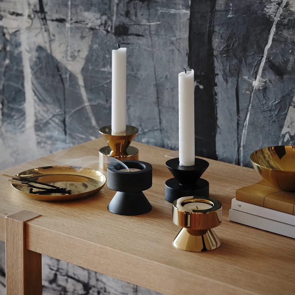Brass candlestick holders and bowl on wooden table with candles and books.