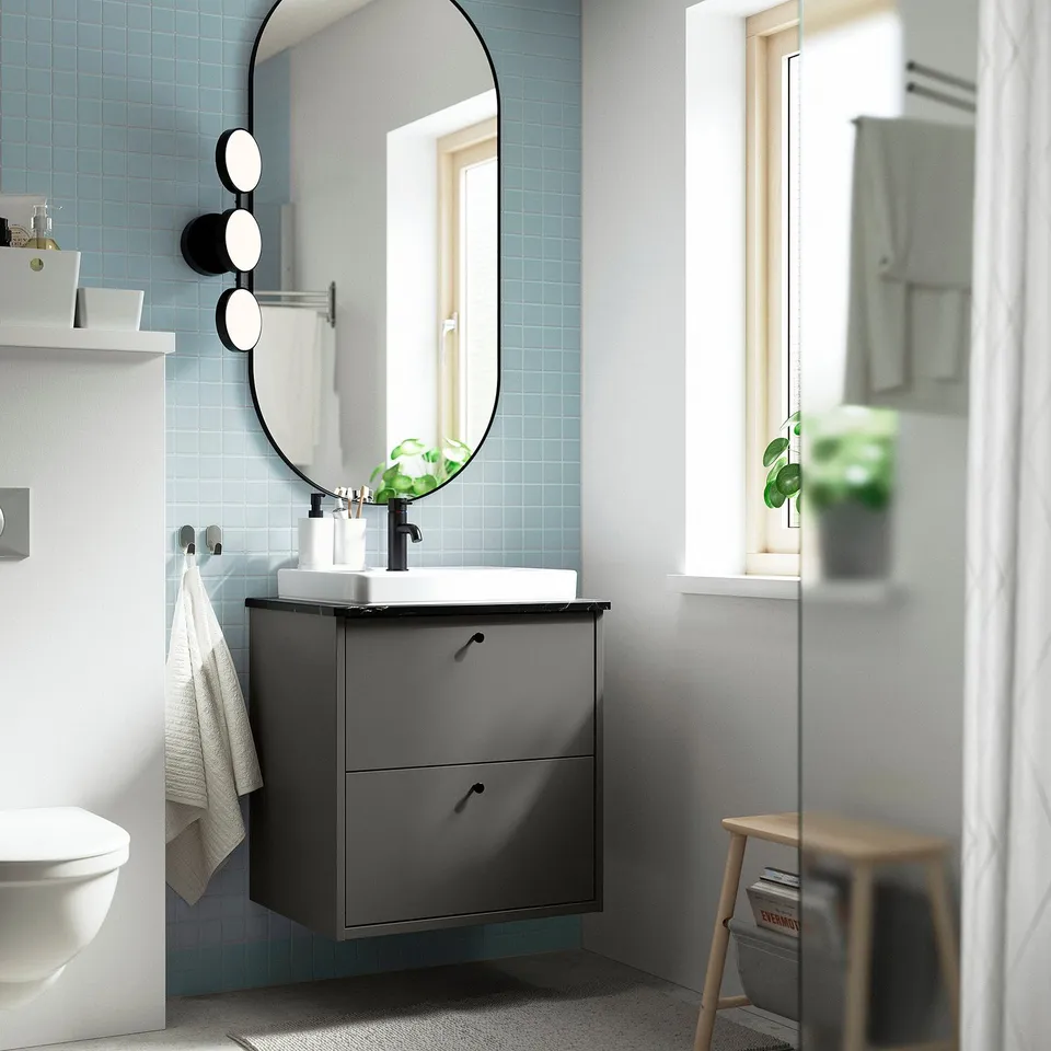 Modern bathroom with dark grey HAVBÄCK vanity, round mirror, blue tiles, white fixtures, and wooden stool.