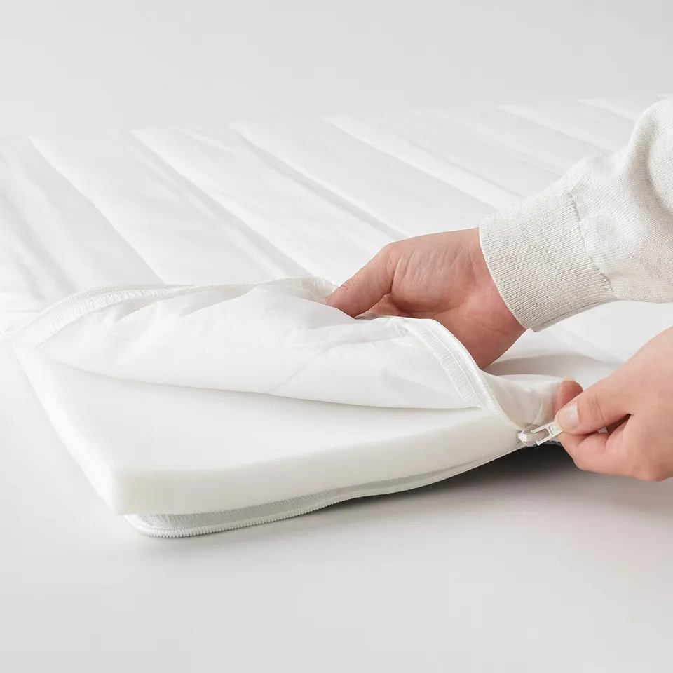 Person zips up white mattress pad on a bed.