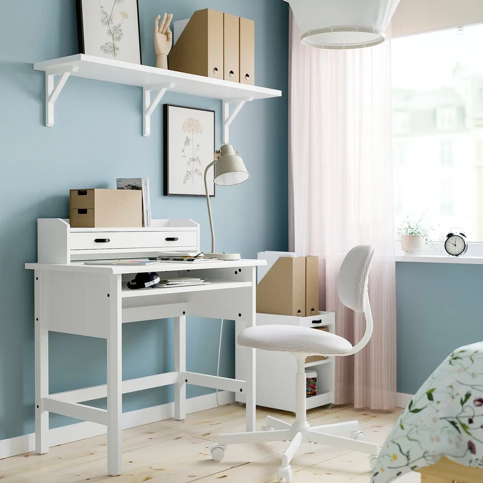 White minimalist desk, perfect for small spaces. Blue wall, pink curtains, chair tucked in, clock & plant on side table.