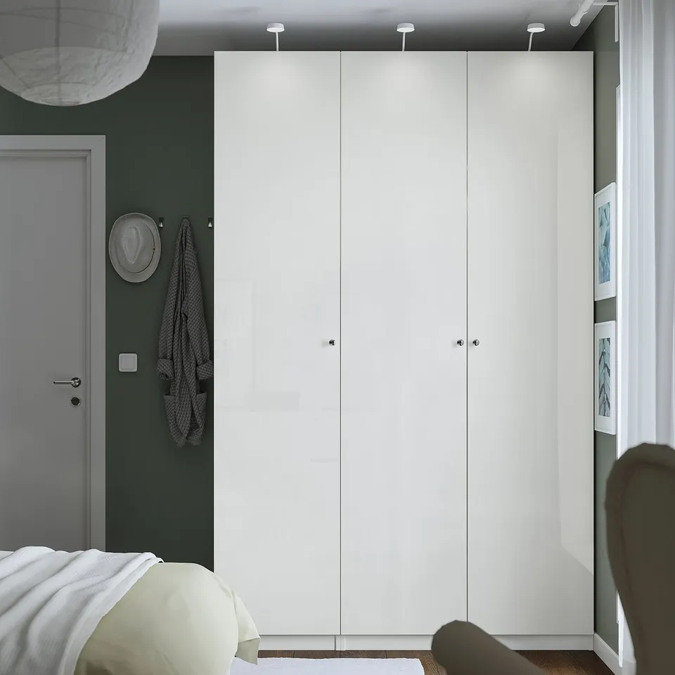 Modern white PAX wardrobe against green wall, taller than grey door, with partial chair and bed.