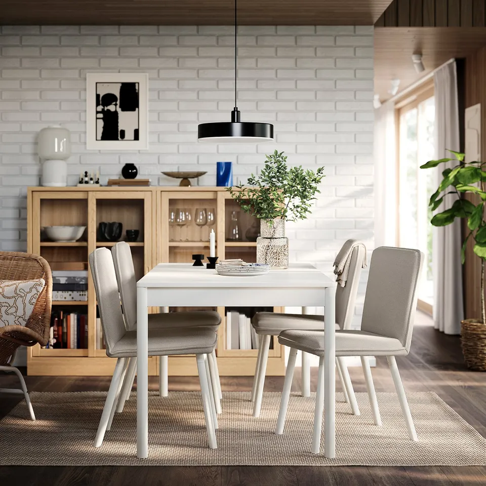 Modern dining with white TONSTAD table, grey chairs, and white brick wall. Black ceiling light, wooden sideboard, and window with white curtains.