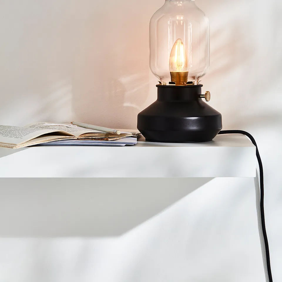 Black TÄRNABY lamp with glass shade on white table.