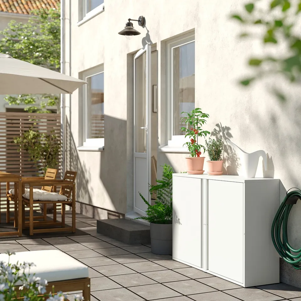 White outdoor cabinet with adjustable shelves near a patio. It has a sleek design and is placed next to a potted plant.