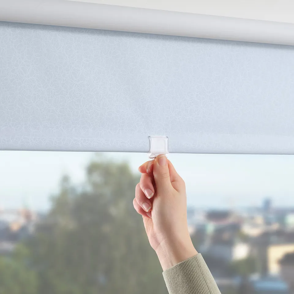 Person pulling white roller blind with circular pattern, blocking light, mounted on window.