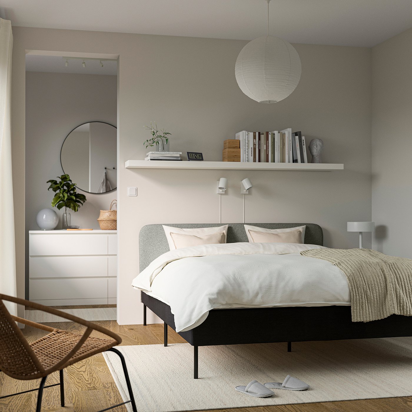 Bedroom with greyish bed, white linens, and neutral decor; wall mirror, plants, and bookshelf.