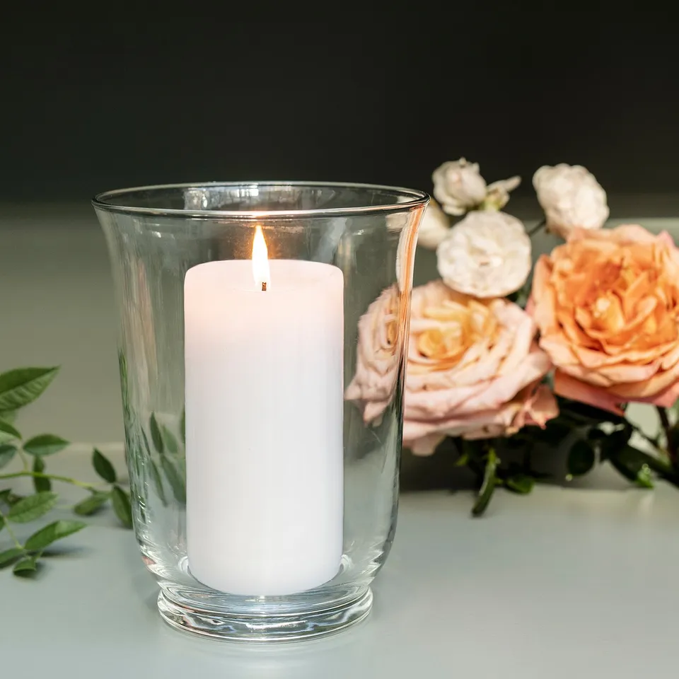 White candle in clear glass vase beside light pink roses.