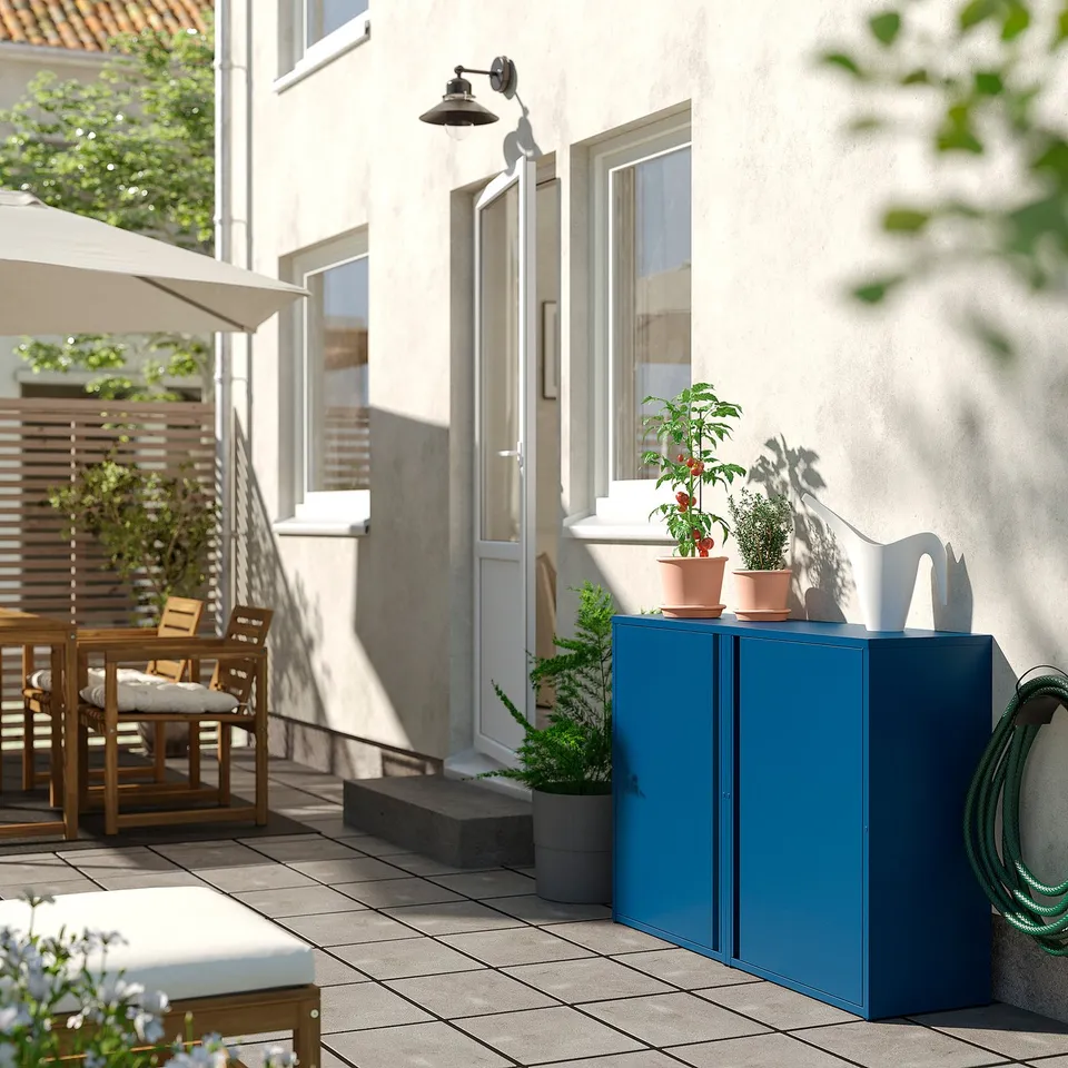 Modern outdoor patio: teal cabinet, plants, dining set, beige house.