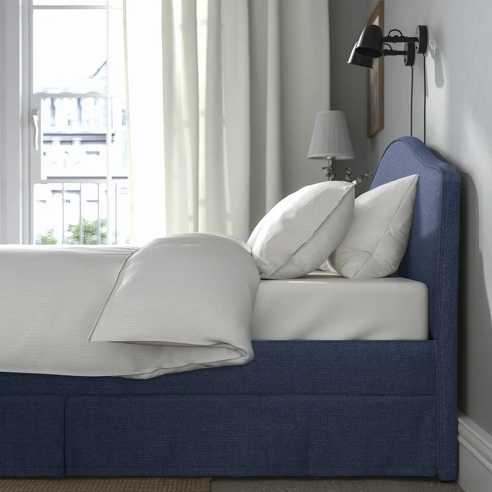 An a bed with a blue RAMNEFJÄLL cover, featuring clean lines, and a lampshade on the wall near the headboard.