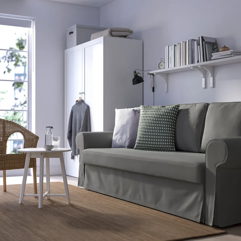 Grey sofa-bed near bookshelf, bright room